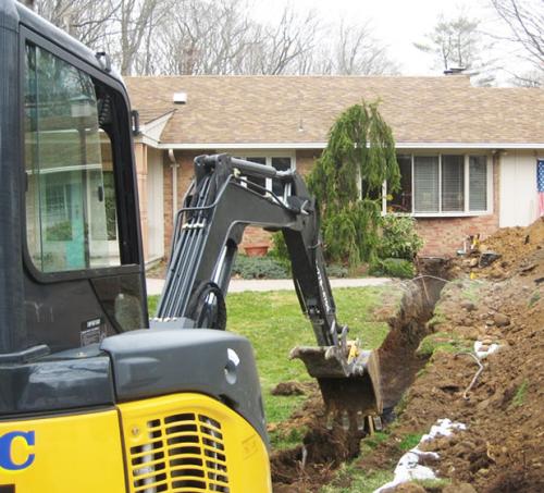 Backhoe digging a trench in front of a house